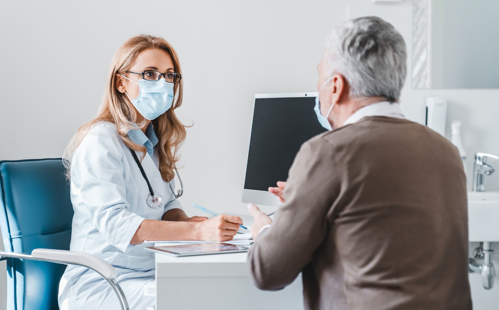 Woman doctor wear protection face mask talking with patient in clinic office